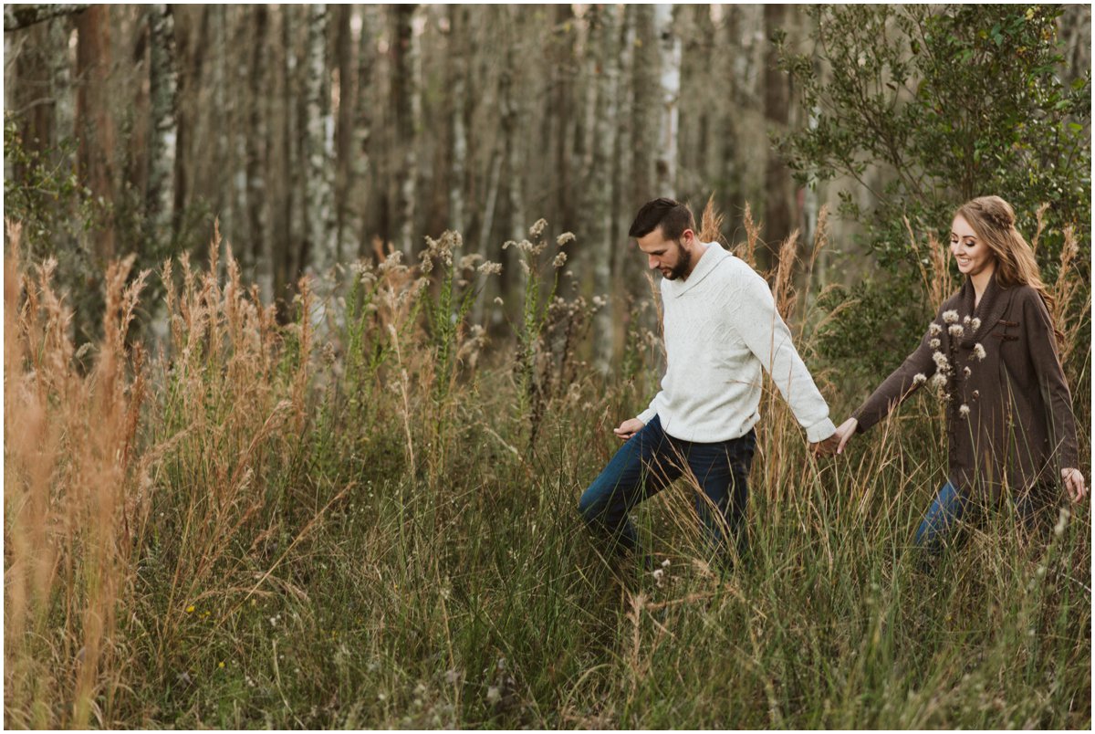 couple holding hands walking through tall grass at Belle Oaks Barn Brooker
