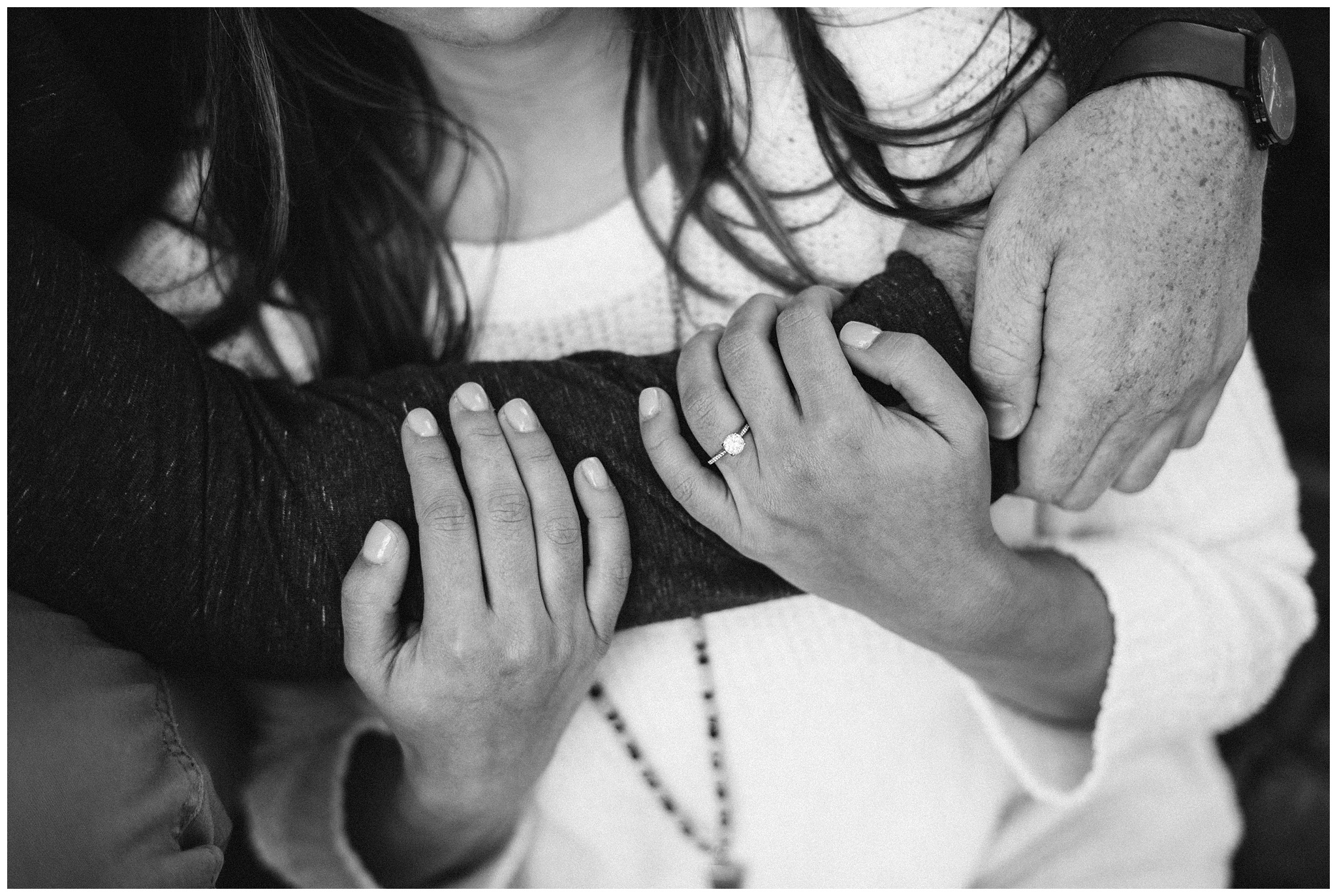 Black and white image of grooms arms around brides chest snuggling